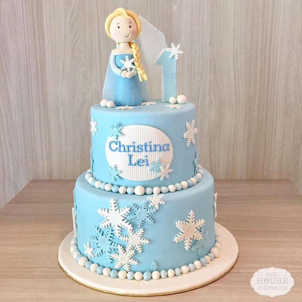 A two-tiered cake adorned with edible pearls, snowflakes cutouts and a figurine of Queen Elsa. Little House of Dreams. Source