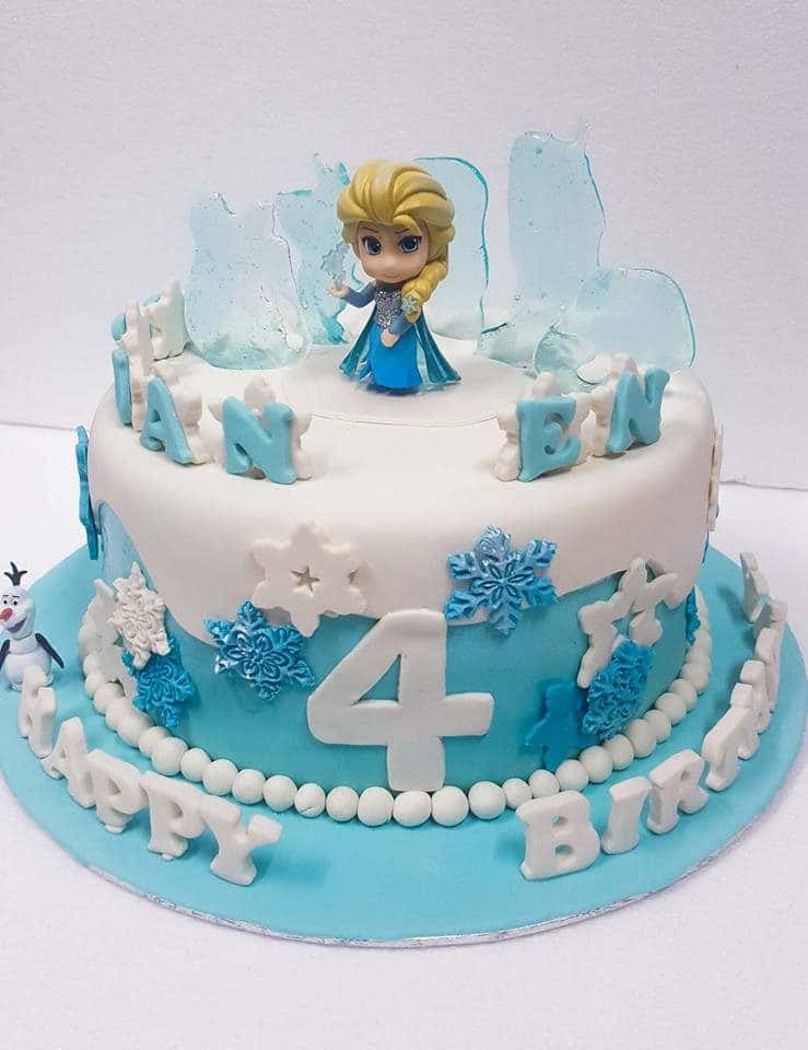 A tall round cake decorated with white and blue fondant cutouts, sugar glass and figurines of Frozen characters. Little Sprinkles. Source