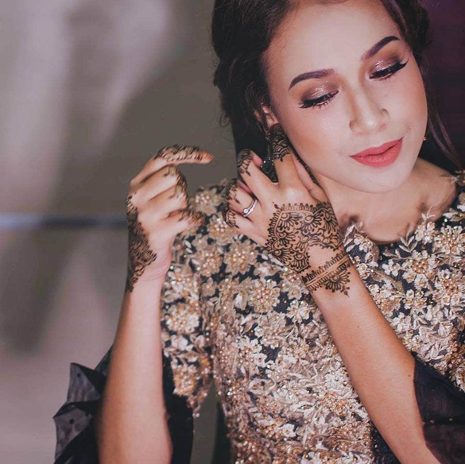 Malay bride in black, white and gold gown adjusts her earrings before wedding ceremony. Photo by Cubic foto